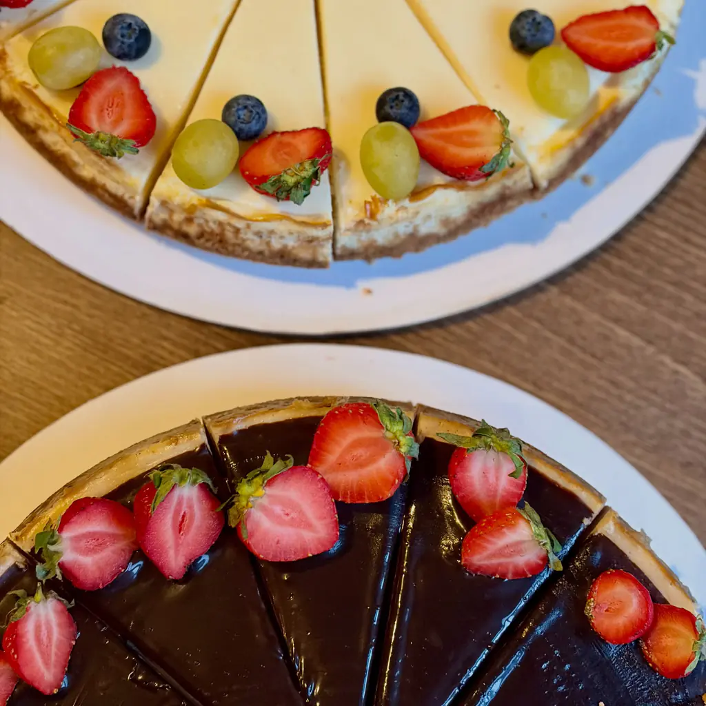 Dva nakrájané cheesecaky zhora: svetlý s jahodami, čučoriedkami a hroznom a tmavý s jahodami